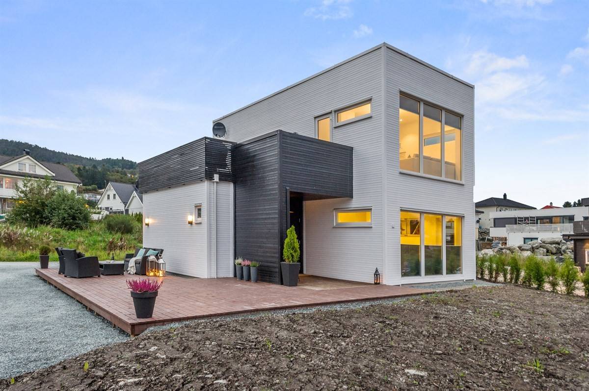 Moderne to-etasjes hus med flatt tak, hvit og svart kledning, store vinduer og terrasse i tre