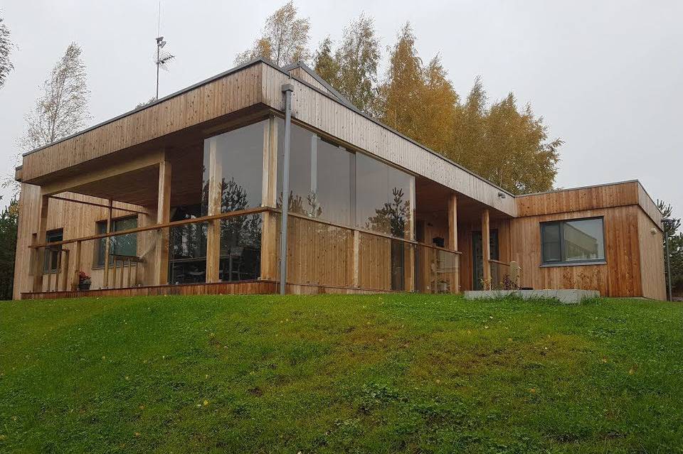 Enetasjes hus med stående trekledning, innglasset overbygd terrasse og gressbakke foran