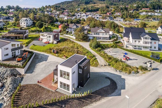 Dronefoto av nytt hvitt og svart trehus med flatt tak i et boligfelt i en åsside