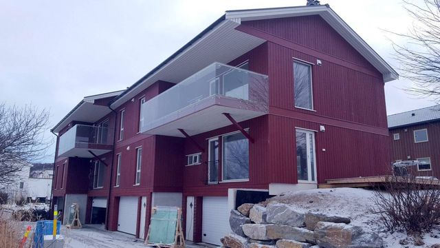 Rød flermannsbolig i tre med glassbalkonger og garasjeporter, snart ferdig, med snø på bakken