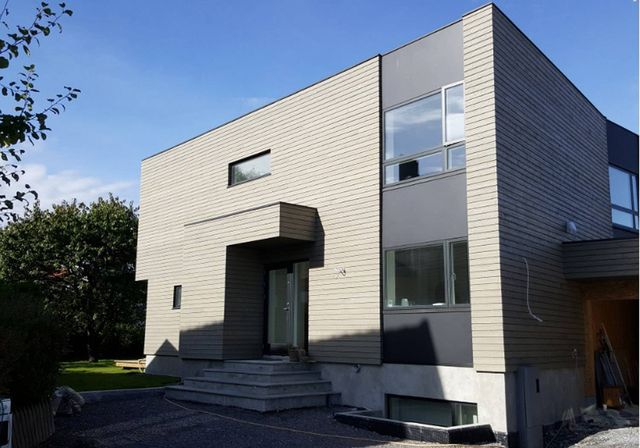 Moderne trehus med flatt tak, grå liggende kledning, overbygd inngang og trapp i betong