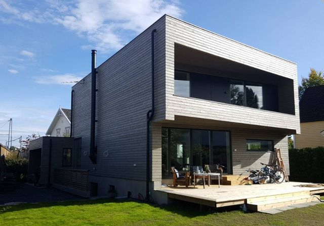 Moderne toetasjes hus med grå liggende trekledning, utkraget overetasje og stor terrasse i hagen