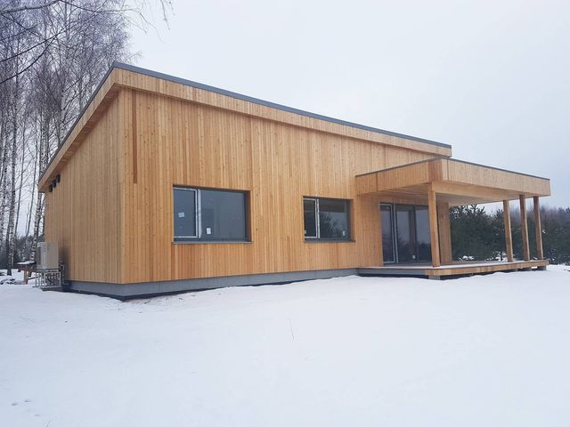 Enetasjes hus med flatt tak og stående ubehandlet trekledning, overbygd terrasse, i snødekt landskap