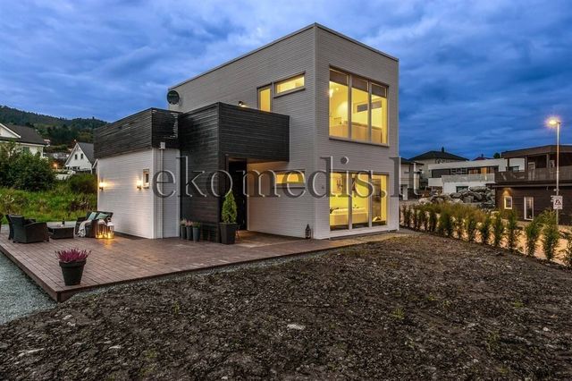 Moderne hvitt og svart trehus i to etasjer i skumringen, med opplyste vinduer og terrasse