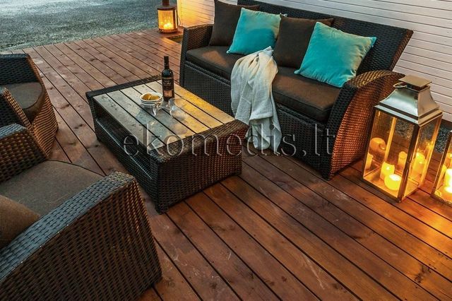 Terrasse i tre med flettede utemøbler, turkise puter og tente lykter mot lys kledning
