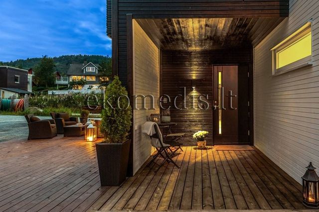 Overbygd inngangsparti med mørk og lys trekledning, terrasse og utemøbler i kveldslys