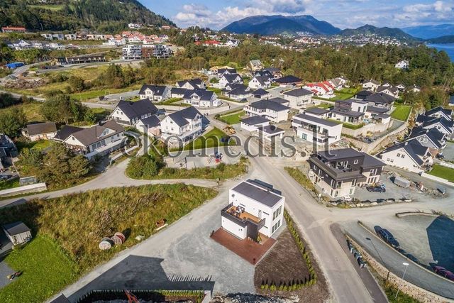 Flyfoto av hvitt hus med flatt tak og terrasse i boligfelt med fjell i bakgrunnen