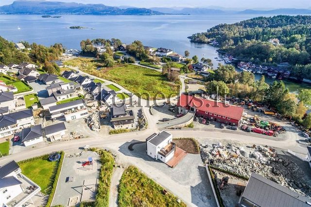 Flyfoto av hvitt hus med flatt tak i boligfelt ved sjøen, nye tomter under opparbeiding
