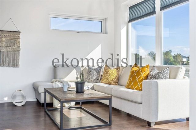 Stuekrok med lys hjørnesofa, gule puter, salongbord og store vinduer