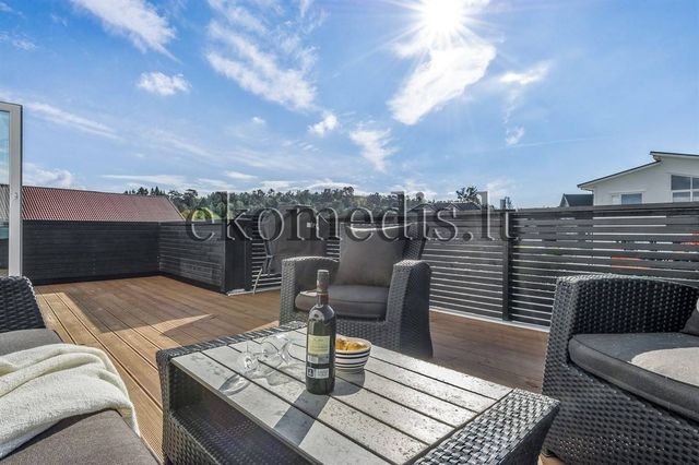 Solrik terrasse med tregulv, mørk levegg og flettede utemøbler