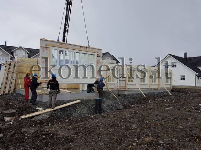 Montører styrer et veggelement med store vindusflater som kranen senker ned på fundamentet