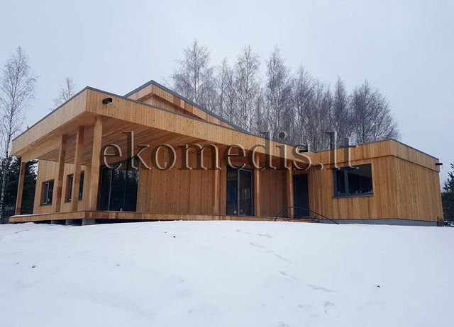 Enetasjes hus med stående trekledning, overbygd terrasse på stolper og store vinduer i snølandskap